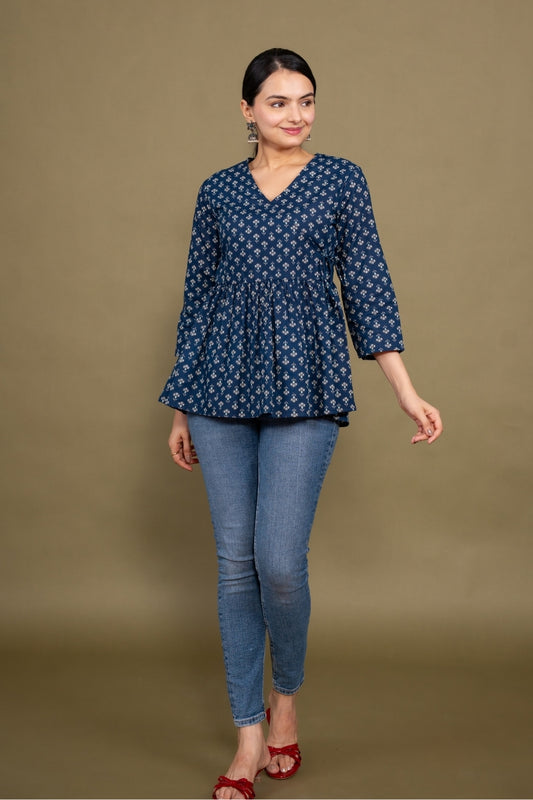 Woman wearing a blue patterned top and jeans against a brown background